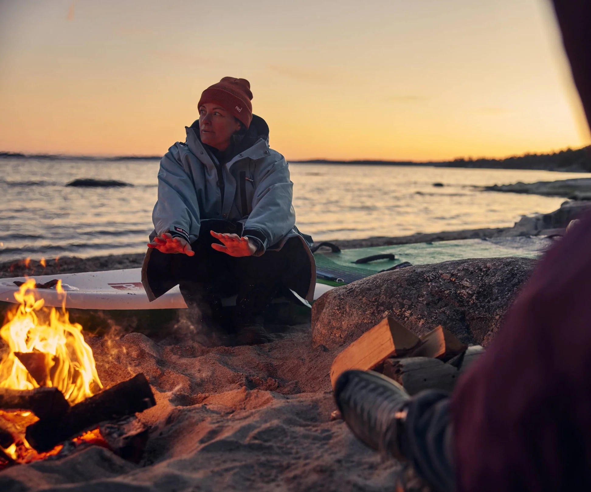A woman sat on the beach warming her hands by a fire