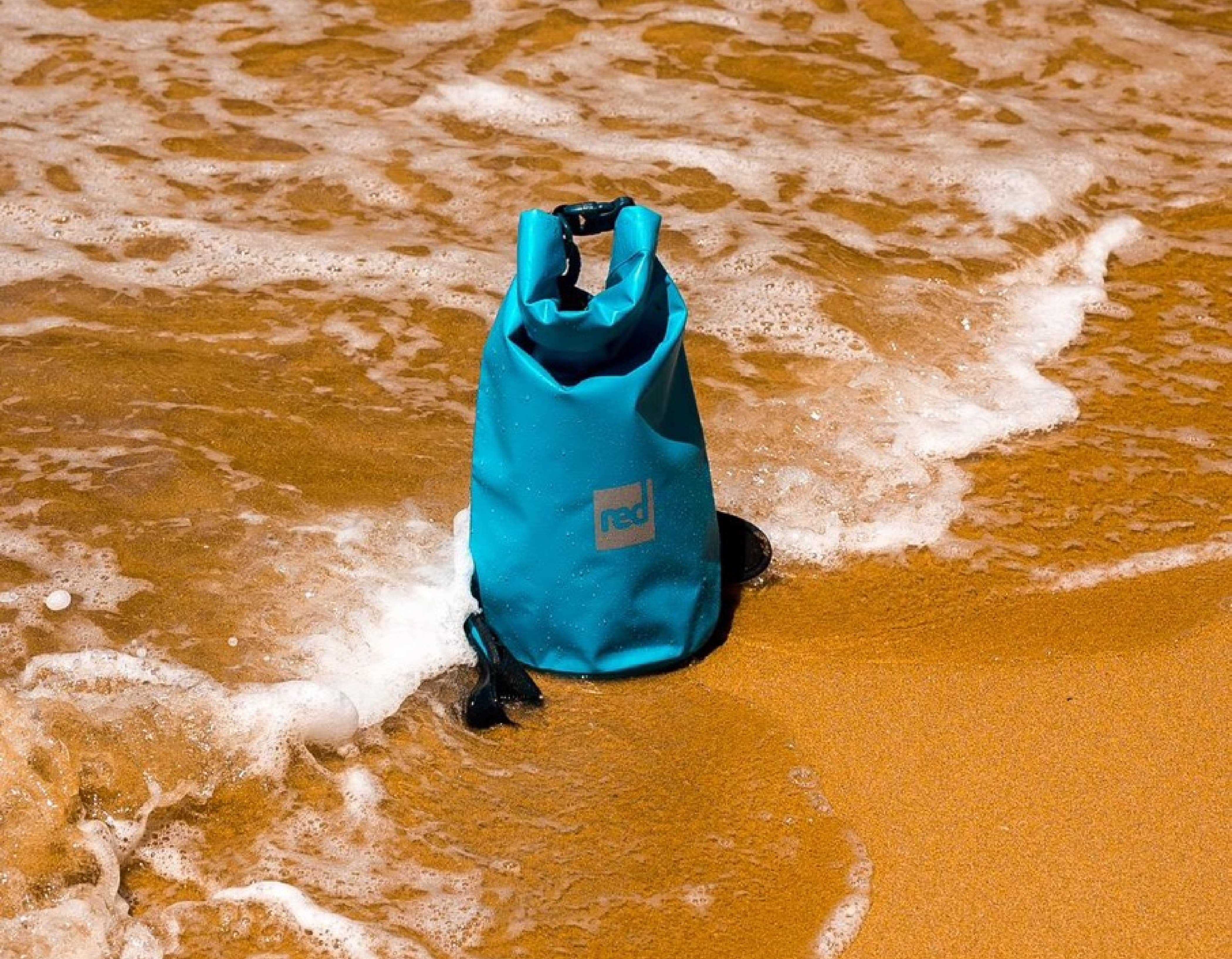A Red Ride Blue 10 Litre Roll Top Dry Bag on the sea shore.