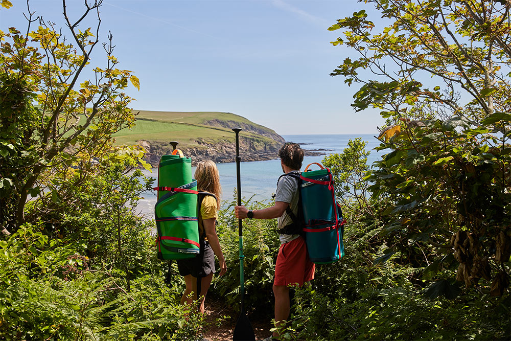 Man and woman carrying Red Original SUP’s whilst looking out to sea