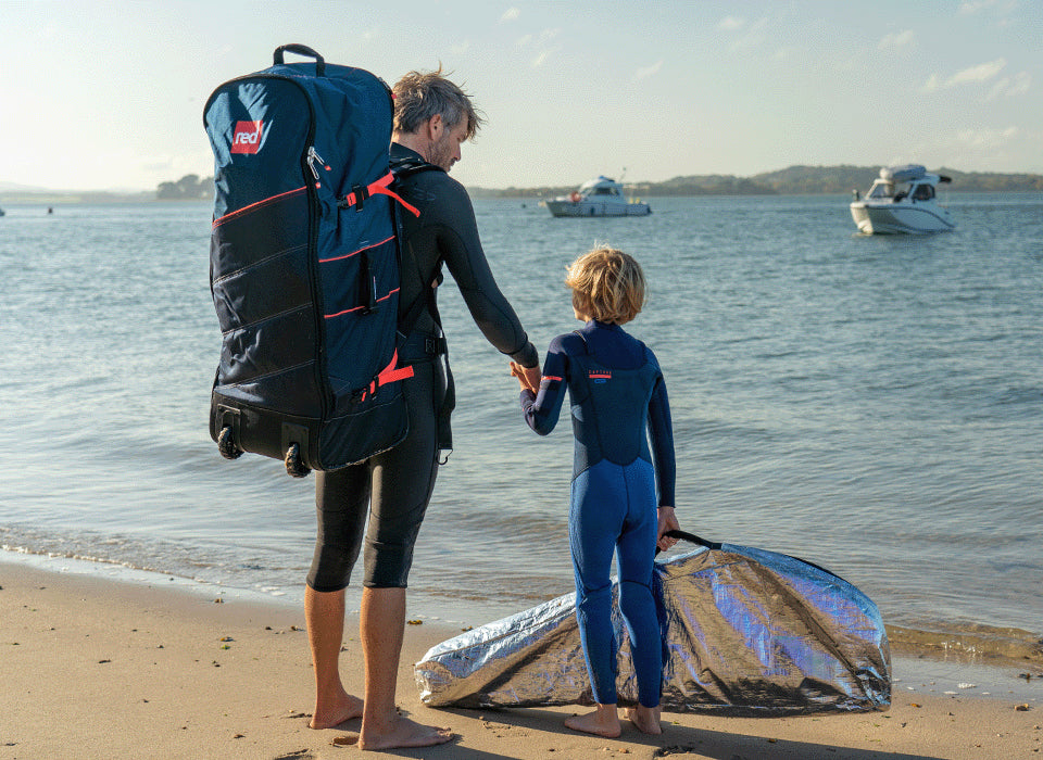 A man and his son holding hands walking along the beach wearing a backpack