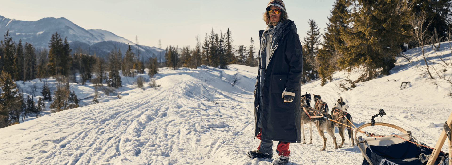 A man hiking in the snow while his husky dogs pull a sled