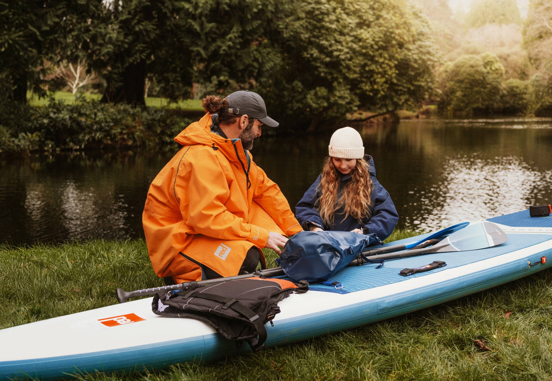 man and child packing equipment into dry bag on red paddle board