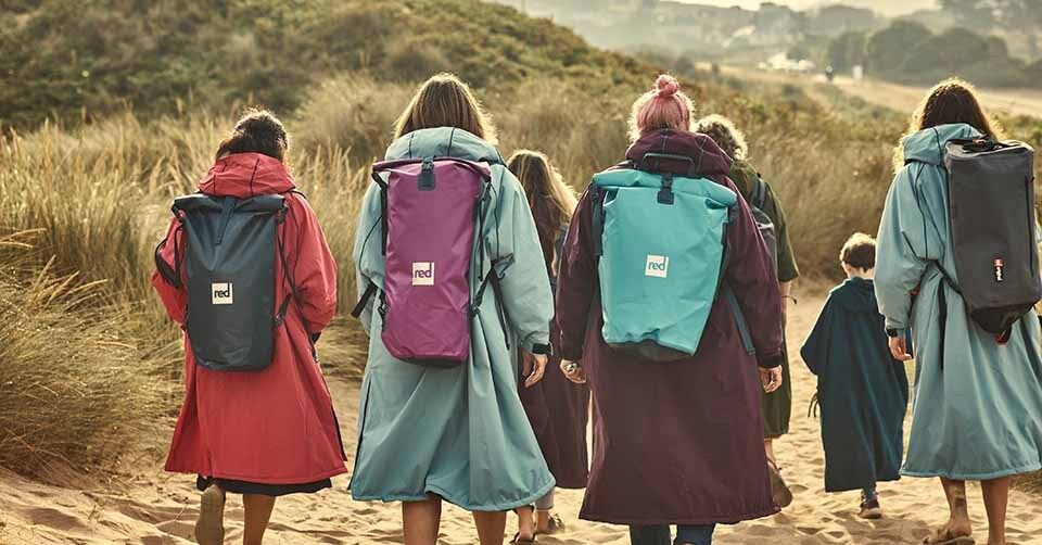 Four women walking along the beach wearing Red Original Pro change robes  