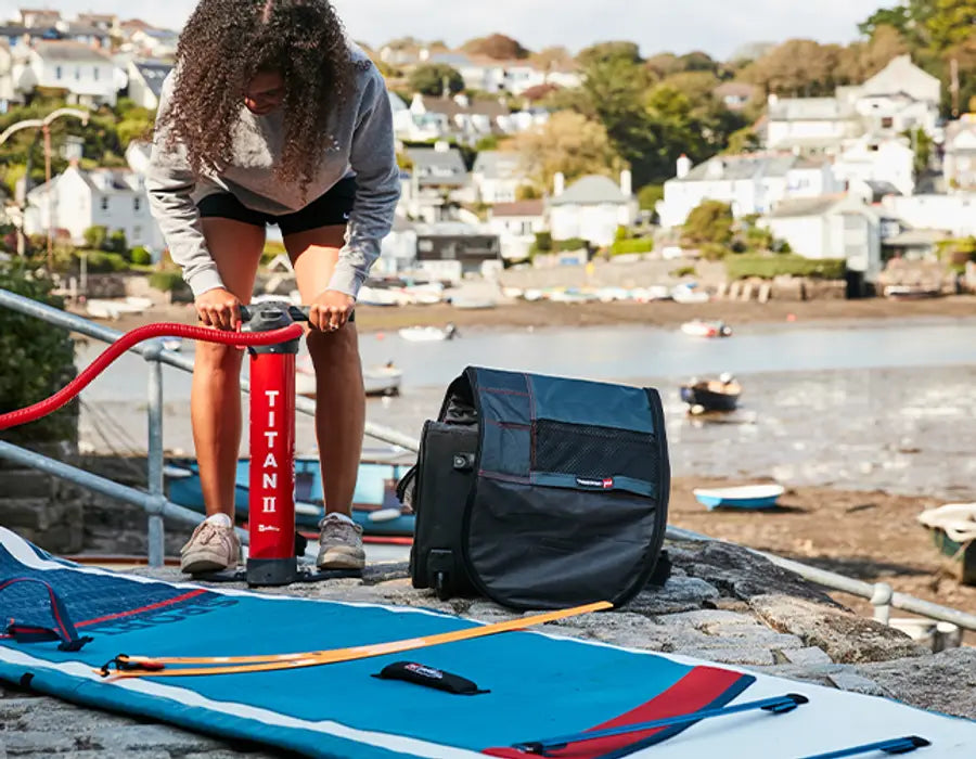 A woman using the Red Titan 2 Pump to pump up her paddleboard by the water