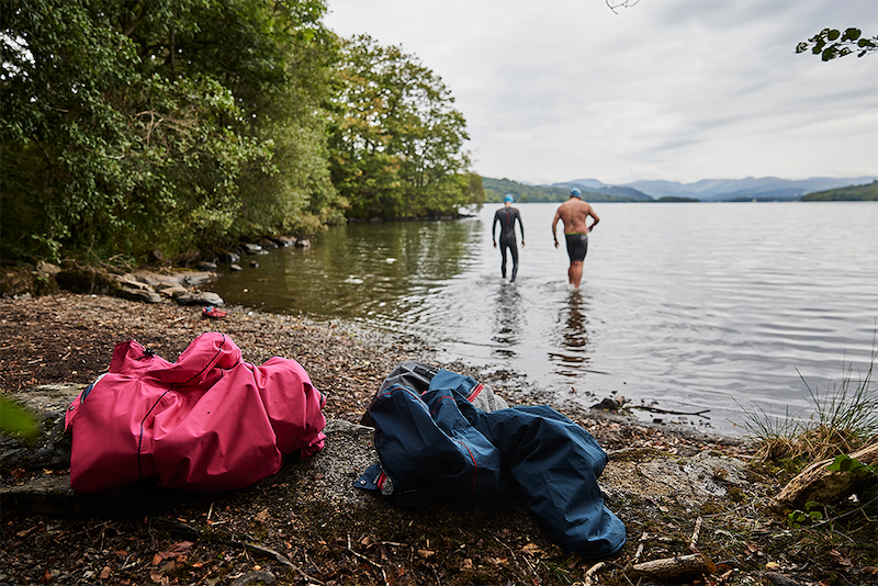 Two men walking into lake to swim