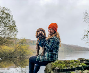 Woman sat with dog near lake on cold winters day