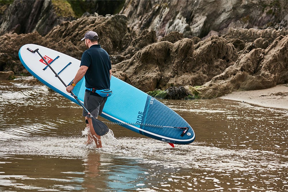 man walking into the sea carrying an inflatable paddle board