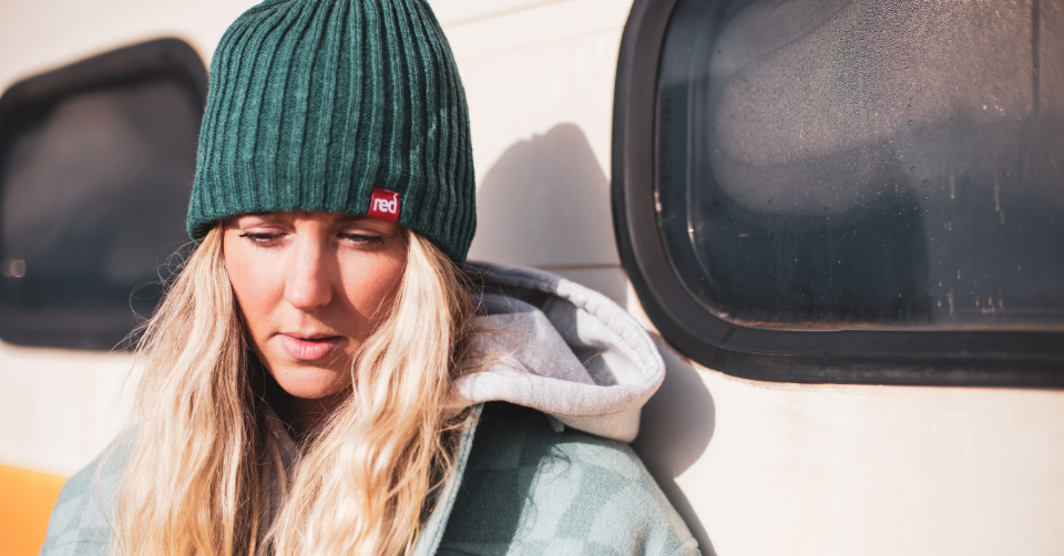 woman wearing teal knitted beanie standing against a campervan