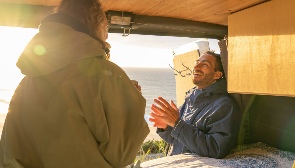 man and woman laughing sat in campervan wearing red original changing robes