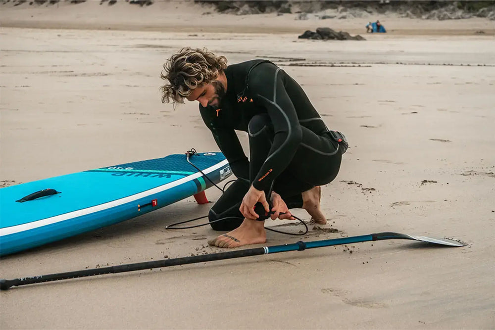 A man attaching the paddleboard safety strap to his ankle on the beach