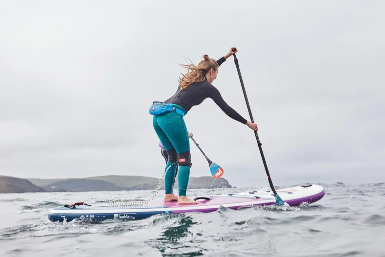 A woman paddleboarding on a choppy ocean