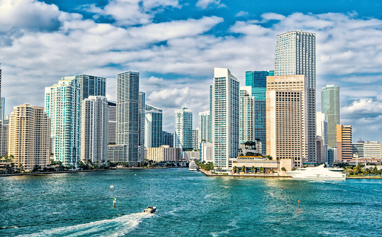 Yachts sail on sea water to city skyscrapers on cloudy blue sky in Miami,