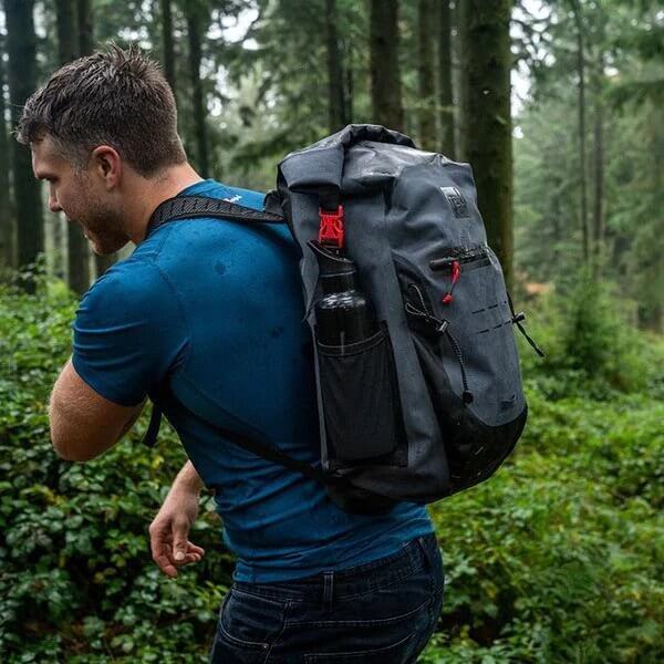 man wearing Red Original Waterproof Backpack whilst walking through woodland area