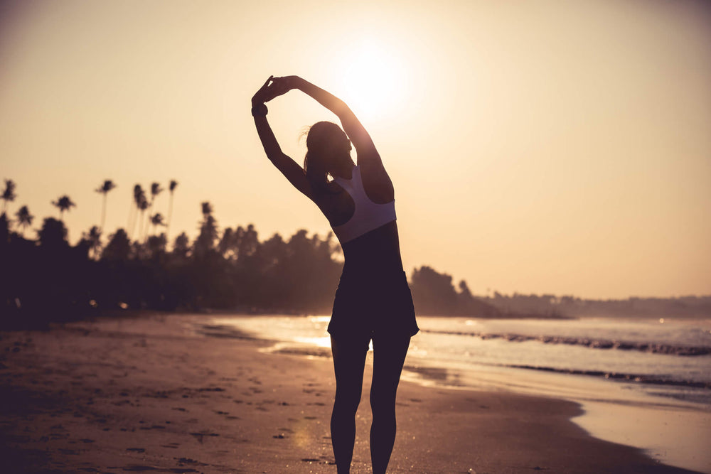 woman doing an overhead stretch on a beach at sunrise