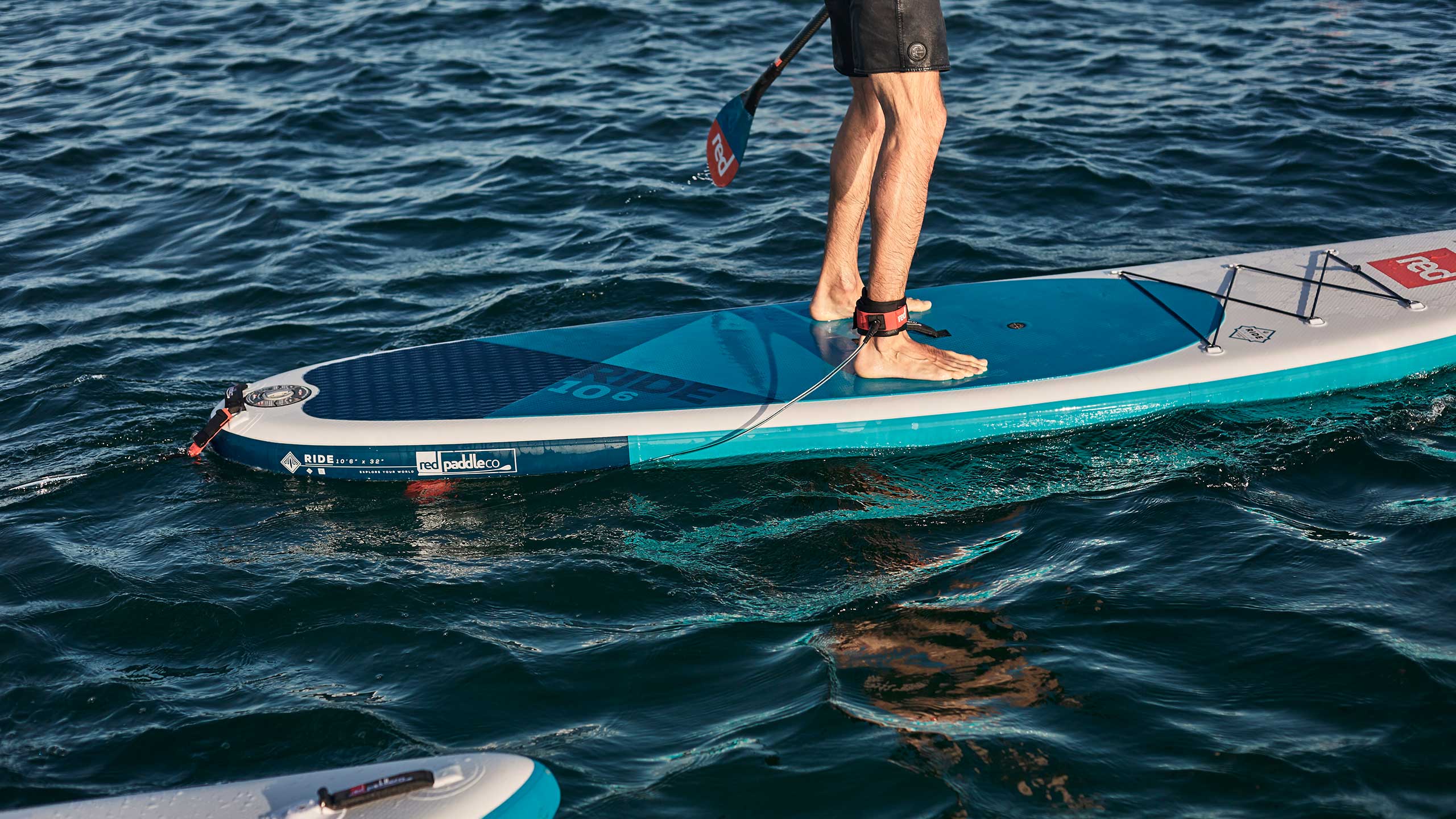 Man paddling in lake using Red original straight SUP leash