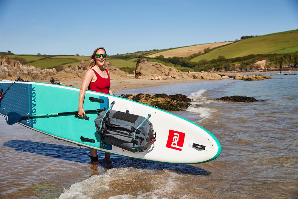 Woman carrying Red Original touring SUP on beach