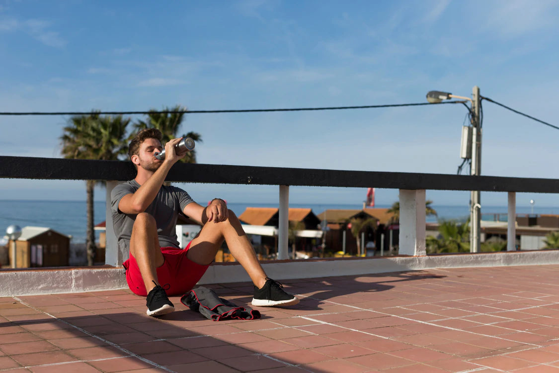 Man sat near beach using insulated stainless steal water bottle