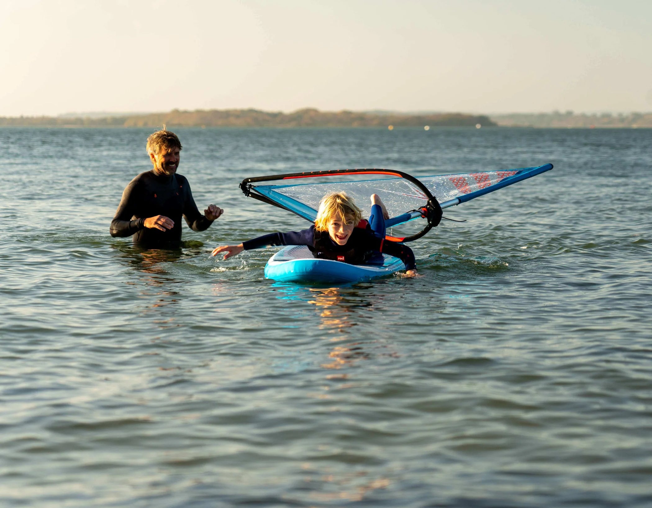 A father and son in the ocean where the son is laying down paddleboarding and the father is paddling in the ocean