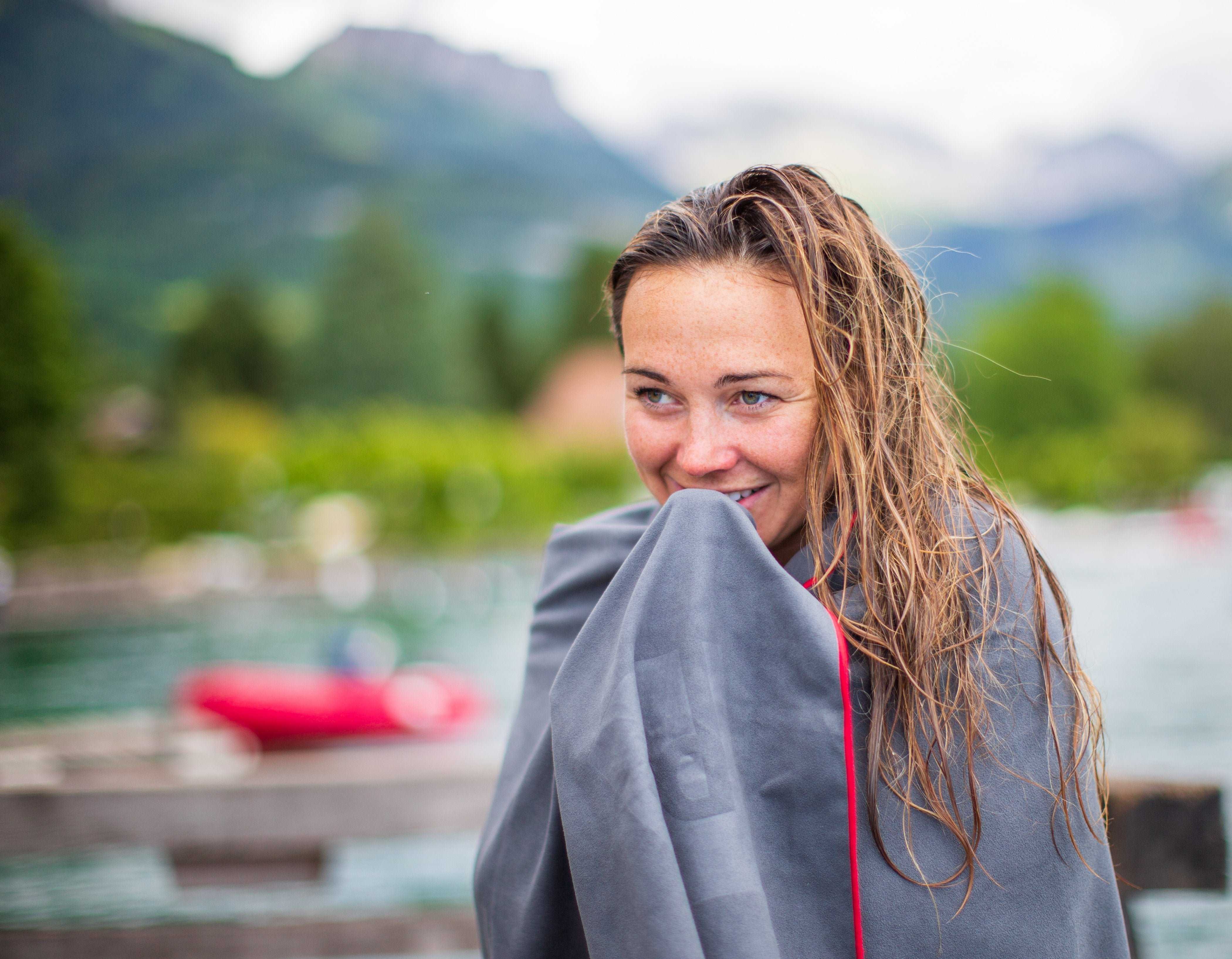 Woman wrapped in a Red Microfibre towel beside a lake.