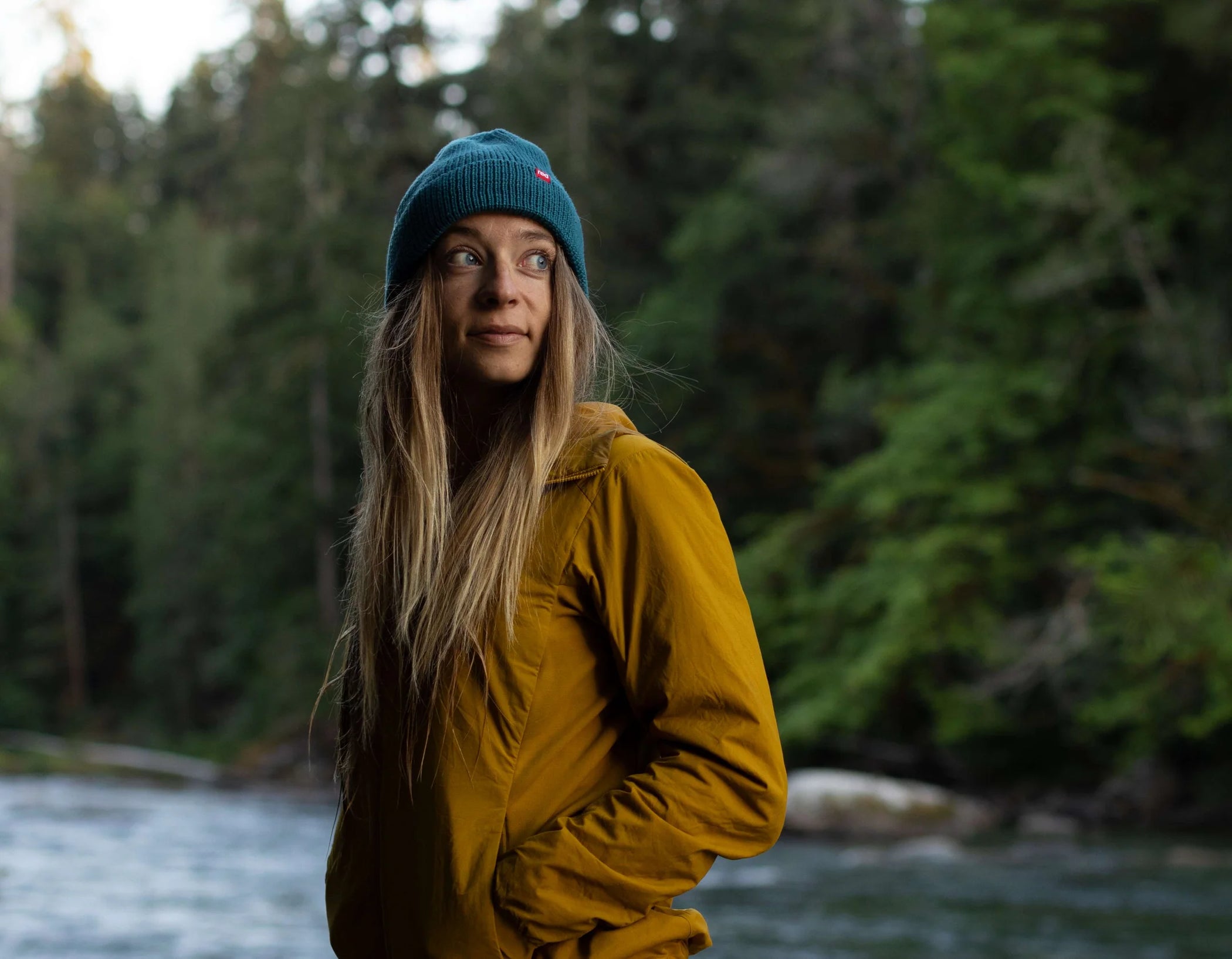 A woman wearing a eddy beanie, stood in front of a beanie, looking to the side