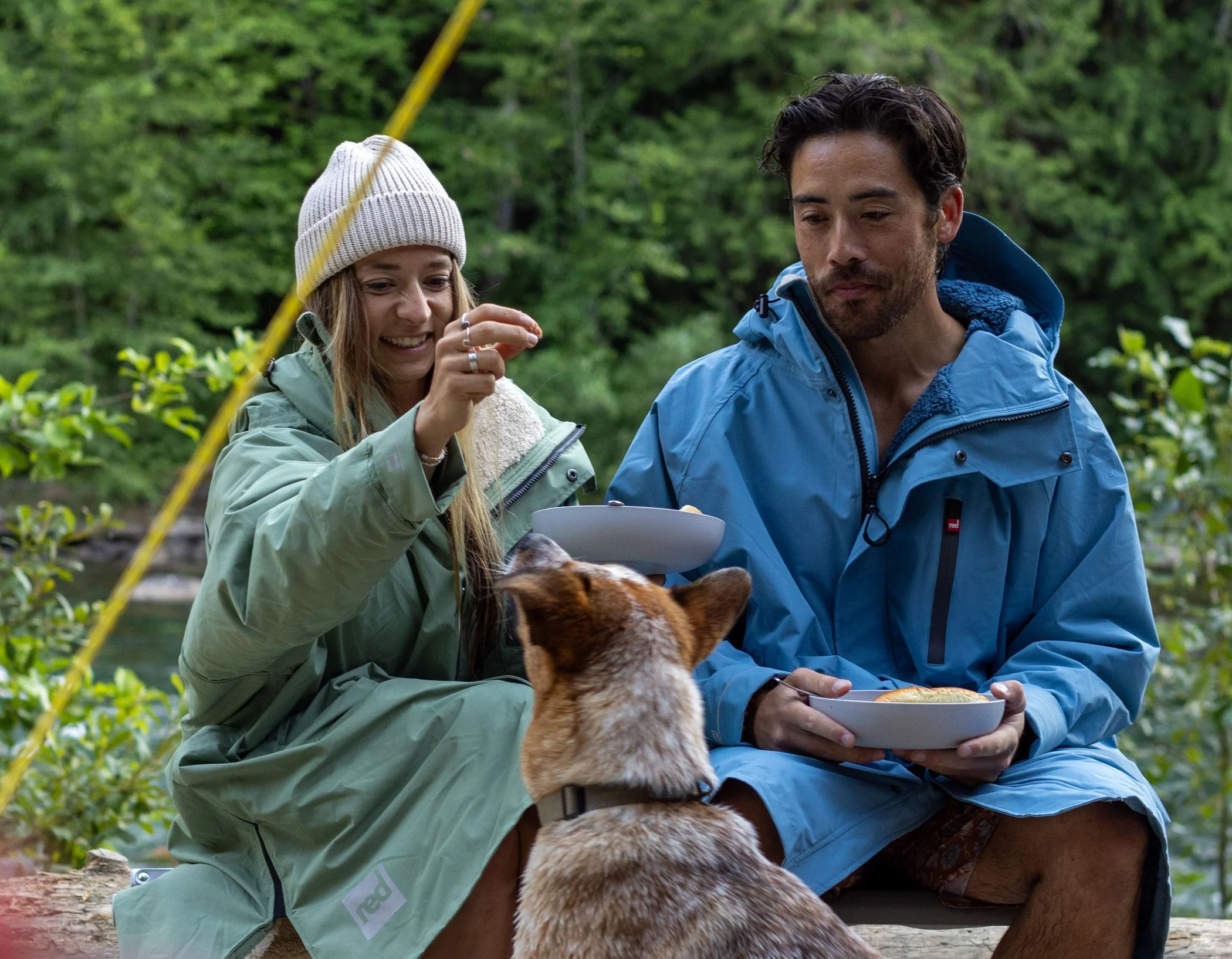 A man and woman sat outside eating, feeding their dog, wearing their long sleeve pro change robe