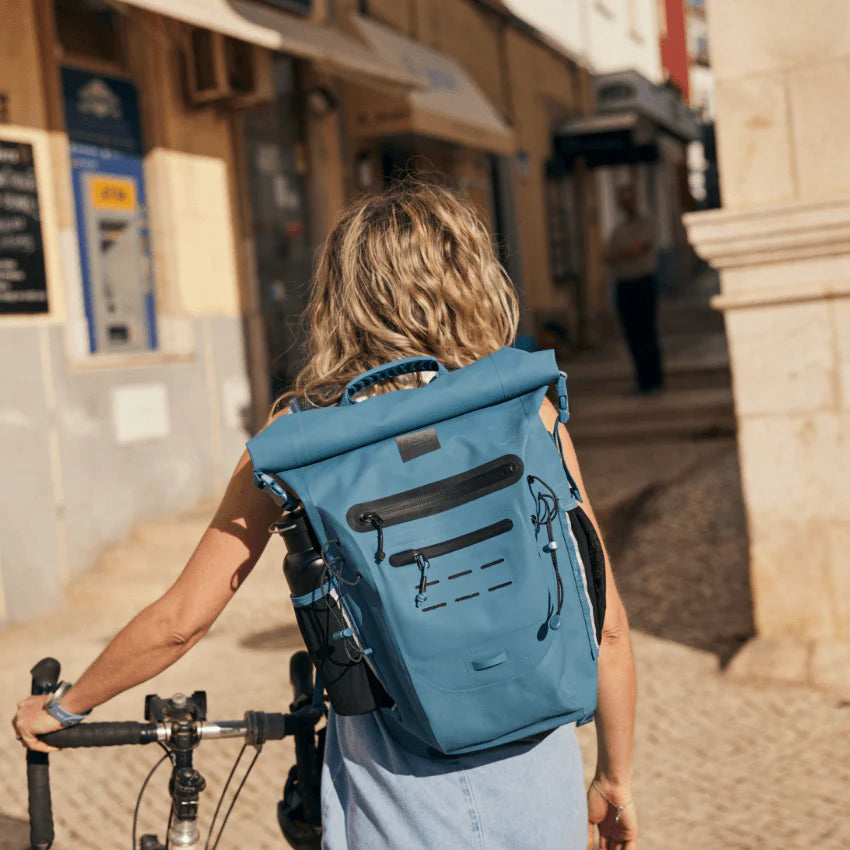 A person pushing their bike along the street wearing a backpack